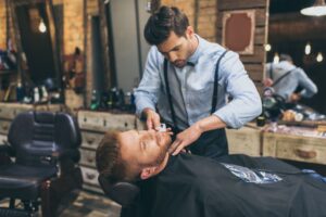 male-barber-trimming-customers-beard-in-barber-sho-YR2WUV3